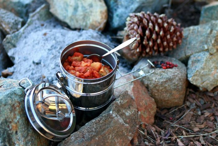 Metal pot and spoon resting on some rocks, essential equipment for base camping. Vaia Magazine