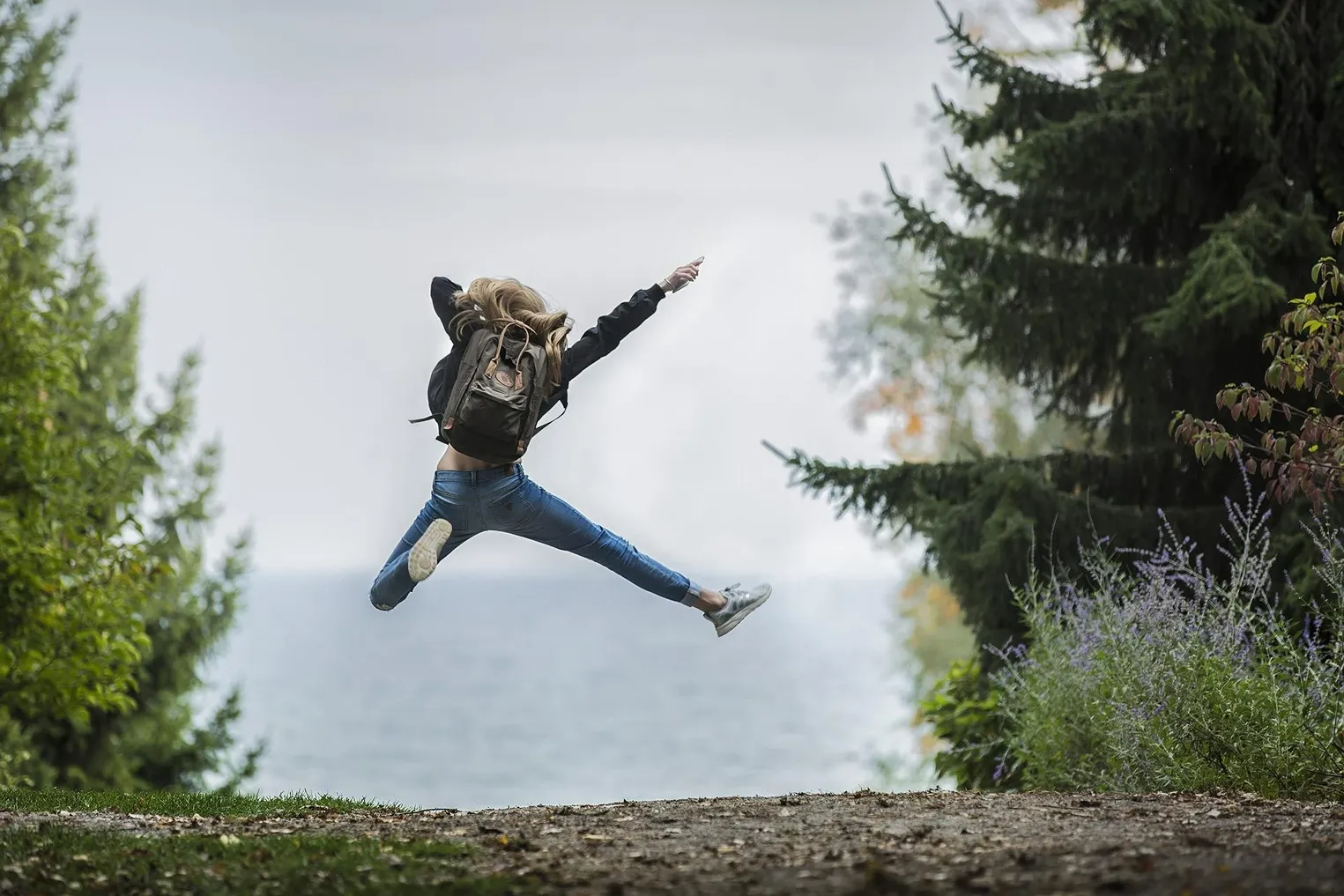 Fear of Failure, Photograph of a woman with a backpack jumping in the forest towards the ocean, Vaia