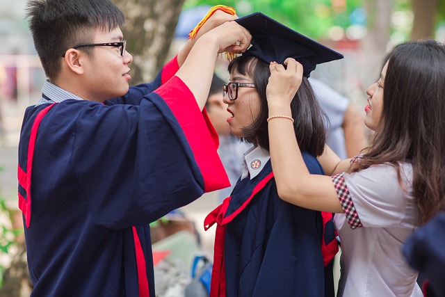 Two students helping a third student with their graduating cap while chatting. Vaia Magazine