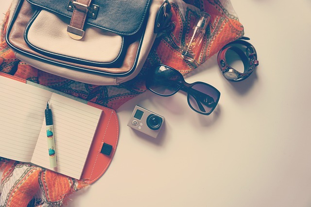 A collection of a backpack, sunglasses, camera, watch, and an open notepad with a pen resting on it. Vaia Magazine