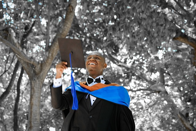 A young master's degree graduate about to throw his cap in the air amongst trees. Vaia Magazine