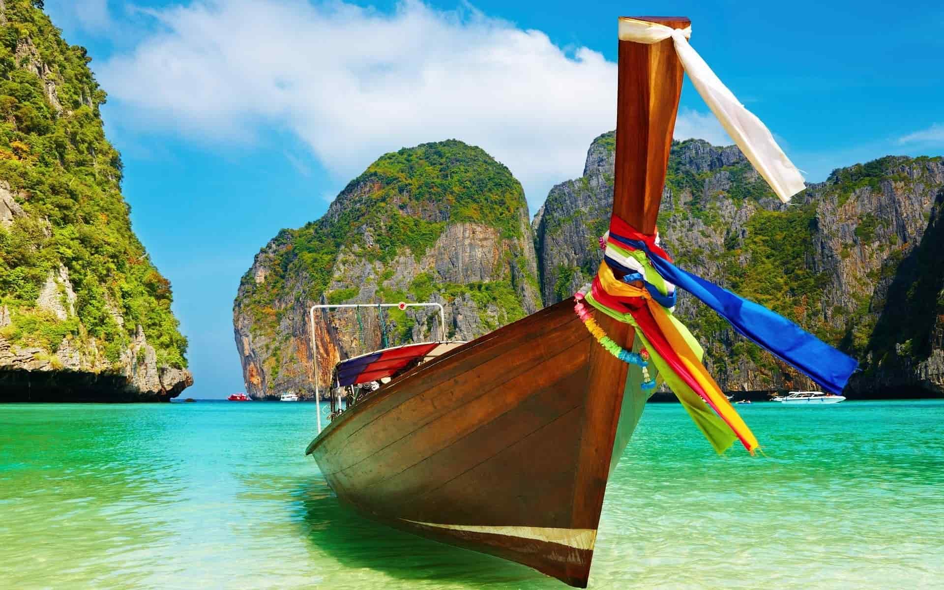 A boat resting in the clear blue ocean with picturesque rocks in the background. Vaia Magazine