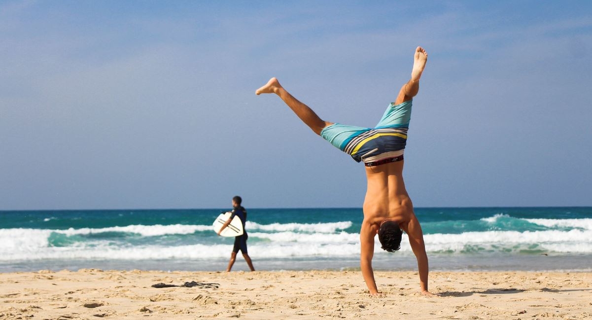 A man doing a handstand by the beach as a quick study break exercise. Vaia Magazine